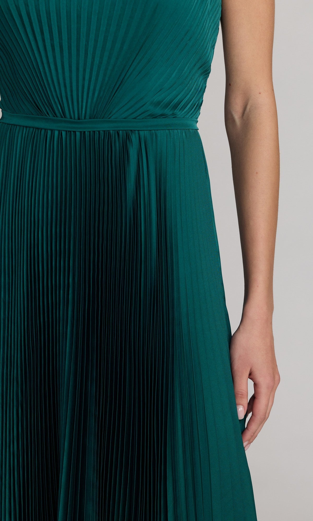 A person is wearing the Mac Duggal 56326 midi party dress, featuring a sleeveless, pleated dark green design with a modest A-line skirt, standing against a plain light background with one arm visible.